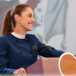 Claudia Sheinbaum sonríe mientras habla desde el podio con el escudo de México durante un evento oficial del Gobierno federal.