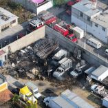 Vista aérea del incendio en un predio de Querétaro con camiones y cabinas calcinadas mientras bomberos trabajan para sofocar restos del fuego.