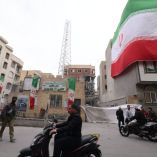 Una enorme bandera iraní ondea en un edificio mientras los iraníes caminan junto a las estructuras dañadas
