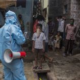 Trabajador sanitario con equipo de protección informa a familias en India durante la pandemia de covid-19 en un barrio urbano con población infantil.