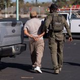 Un inmigrante documentado detenido por el Servicio de Inmigración y Control de Aduanas de Estados Unidos (ICE), camina esposado mientras un agente lo sujeta del brazo en el estacionamiento de un Home Depot en Tucson, Arizona.