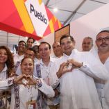 Funcionarios y promotores de Puebla posan en stand del Tianguis Turístico con vestimenta tradicional y logotipo del estado visible en el recinto