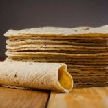 Una tortilla hecha taco y al fondo tortillas apiladas.