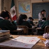 Salón de clases con estudiantes durante una evaluación, libros y exámenes reprobados en primer plano, imagen que representa el retroceso educativo señalado en los resultados PISA.