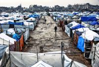 Men walk along a muddy alley at a makeshift camp sheltering displaced Palestinians after heavy rains in the Zeitoun neighbourhood of Gaza City on December 11, 2025. The United States, alongside Qatar and Egypt, secured a truce in Gaza that came into effect on October 10 and has mostly halted two years of war between Israel and Palestinian militant group Hamas. (Photo by Omar AL-QATTAA / AFP)