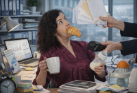 Mujer en oficina con un croissant en la boca mientras sostiene café y un biberón, recibe documentos y atiende tareas laborales frente a una computadora, imagen que simboliza la carga mental y la doble jornada de las madres trabajadoras.