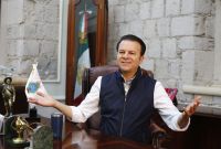 Esteban Villegas Villarreal sentado en su oficina en Durango, con bandera de México al fondo y escritorio con objetos institucionales