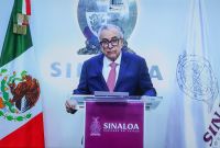 Rubén Rocha Moya, Gobernador de Sinaloa, en conferencia de prensa. Viste traje azul, corbata fucsia y gafas.