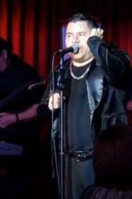 Alejandro Zúñiga interpreta sus canciones durante una presentación en vivo, acompañado por músicos, ante el público y con iluminación escénica.