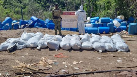 Agentes de la Semar resguardan decenas de costales con metanfetamina frente a barriles de químicos en un laboratorio clandestino en Sinaloa.