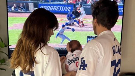 Barbara Palvin y Dylan Sprouse, vestidos con camisetas de los Dodgers, sostienen a su primera hija frente al televisor.