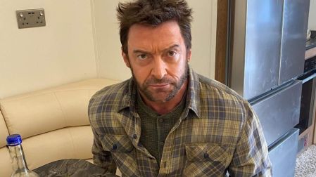 Hugh Jackman caracterizado como Wolverine, con barba y camisa a cuadros, sentado frente a una mesa con comida.