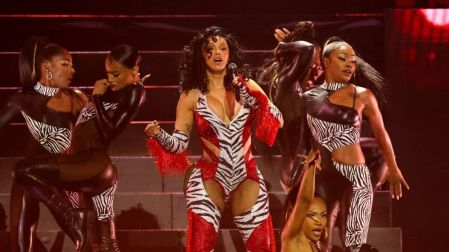 Cardi B canta con un traje rojo y estampado de cebra, acompañada de bailarinas durante una presentación en vivo.