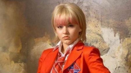 Angélique Boyer como Vico Paz en Rebelde, con cabello rubio corto, flequillo rosa, saco rojo y corbata escolar.