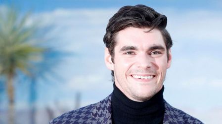 RJ Mitte, actor de Breaking Bad y exnovio de Saint Sasha, sonríe con saco estampado y suéter negro de cuello alto.