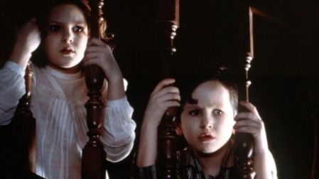 Anne y Nicholas Stewart, personajes de Los otros, observan asustados entre los barrotes de una escalera de madera.