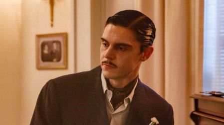 Evan Peters con cabello peinado hacia atrás, bigote y traje oscuro junto a un piano en American Horror Story.