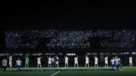 Jugadores de Pumas durante el Himno del equipo con el escudo de los universitarios iluminado por la luz de los celulares. (Mexsport).