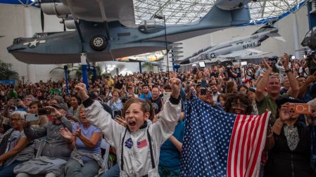 Un niño pequeño, vestido de astronauta, acompaña a una mujer que ondea una bandera mientras celebran el amerizaje de la tripulación en el Océano Pacífico.