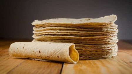 Una tortilla hecha taco y al fondo tortillas apiladas.