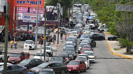 Larga fila de vehículos, incluyendo taxis y un Vocho rojo, bloqueando una avenida principal en Tuxtla Gutiérrez cerca de un establecimiento Ceramat, esperando gasolina de la CNTE.