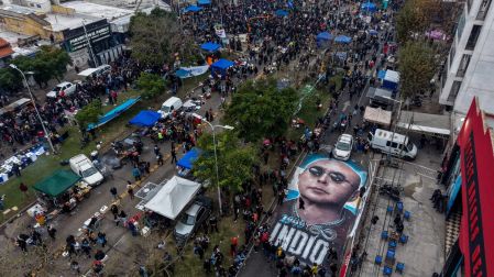This aerial view shows fans next to a huge painting on the street depicting the late Carlos Alberto "Indio" Solari, the iconic Argentine rock musician and former lead singer of Patricio Rey y sus Redonditos de Ricota, as they wait to pay their respects to the coffin with his remains at Villa Dominico, Buenos Aires Province, Argentina, on June 7, 2026. The singer died in Parque Leloir, Buenos Aires Province, on June 5 at the age of 77. (Photo by Tomas CUESTA / AFP)