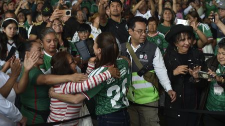 Claudia Sheinbaum, de espaldas usando la playera de la Selección Nacional con el número 26, abraza a una mujer del público en el Fan Fest del Deportivo Los Galeana.