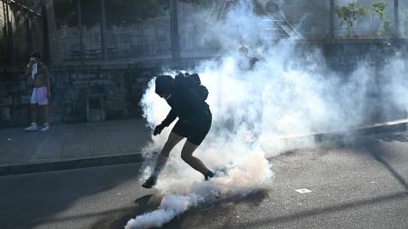 Manifestantes reaccionan junto a una granada de gas lacrimógeno
