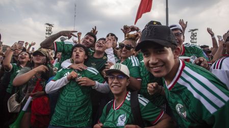 Grupo de jóvenes aficionados abrazados y sonriendo con la camiseta de la Selección Mexicana en una celebración masiva.