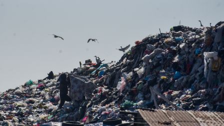 Gran montaña de basura acumulada en un vertedero con aves volando alrededor, mostrando la crisis de residuos.