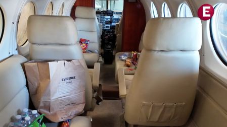 Interior del avión del Mayo Zambada mostrando los asientos de pasajeros, bolsas de botanas sobre los sillones y una bolsa grande de evidencia pericial.