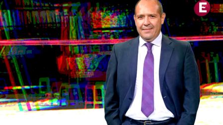Retrato del periodista Alejandro Leyva Aguilar vistiendo traje oscuro y corbata morada sobre un fondo abstracto de colores.