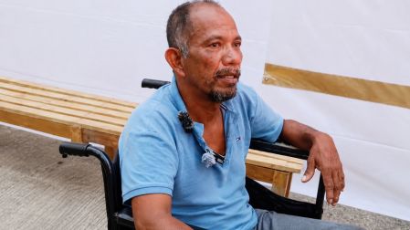 Daniel Guerrero, pescador mayor con playera azul, sentado en una silla de ruedas con micrófonos en el pecho mientras da su testimonio tras el rescate.
