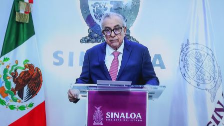 Rubén Rocha Moya, Gobernador de Sinaloa, en conferencia de prensa. Viste traje azul, corbata fucsia y gafas.