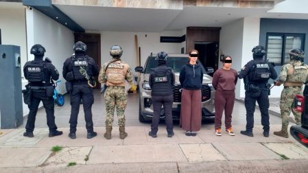 Dos mujeres detenidas durante los cateos contra el CJNG, custodiadas por elementos de la Marina, FGR y fuerzas especiales frente a una residencia.