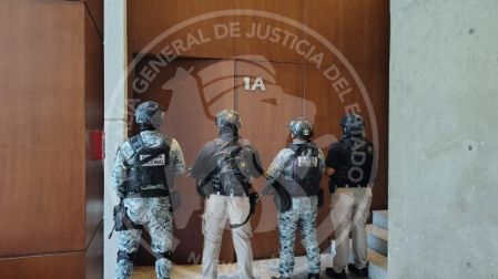 Elementos de la AEI y Guardia Nacional con equipo táctico custodiando puertas de madera en el interior del inmueble cateado.
