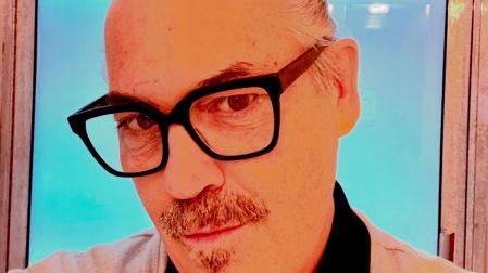 Retrato de Duncan Sheik con lentes negros frente a un fondo azul.