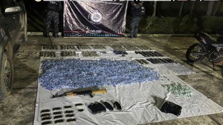 Miles de envoltorios azules y verdes con supuesta droga, junto a un arma larga y múltiples cargadores, expuestos sobre una lona blanca durante un operativo nocturno custodiado por autoridades en Chiapas.