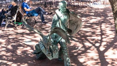 Estatua de Edgar Allan Poe en Baltimore junto a una escultura de un cuervo con las alas extendidas.