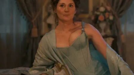 Ruth Gemmell como Violet Bridgerton, sentada sobre una cama con vestido azul claro y chal en una escena de la serie de Netflix.