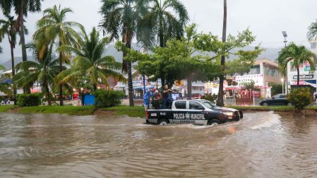 Patrulla de la Policía Municipal de Acapulco transitando por una calle inundada con personas en la parte trasera del vehículo.
