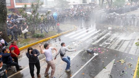 Jóvenes arrojan piedras hacia una línea de policías antimotines bajo chorros de agua a presión durante los disturbios en Guadalajara.