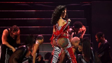Cardi B canta con traje rojo y estampado de cebra, rodeada de bailarines durante un espectáculo musical.
