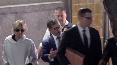 Selma Blair con sudadera blanca y lentes oscuros, acompañada de varios hombres al salir de un edificio en Nueva York.