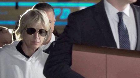 Selma Blair con sudadera blanca y lentes oscuros, acompañada por varios hombres, uno de ellos vestido de traje negro.