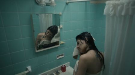 Cazzu con cabello oscuro mojado y toalla blanca frente al espejo de un baño con azulejos turquesa en el video Con otra.¿Te gusta esta personalidad?