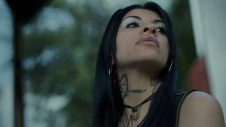 Cazzu con cabello negro largo, aretes de aro, tatuajes en el cuello y collar de corazón en el videoclip de Con otra.