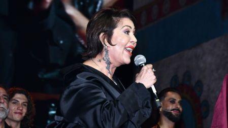 Alejandra Guzmán con atuendo negro y tatuaje en el cuello, hablando con un micrófono durante un evento musical.