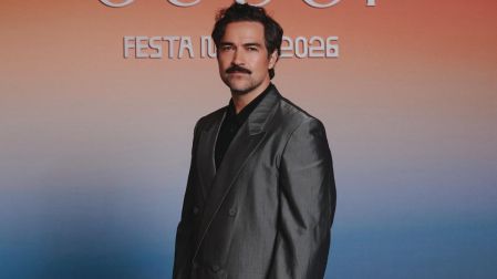 Alfonso Herrera con traje gris y camisa negra posa frente a un fondo de Gucci durante un evento de la marca en 2026.