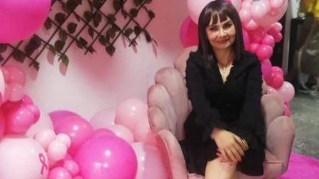 Bettina Salazar, Olga Sana, sentada en un sillón rosa con vestido negro, rodeada de globos rosas y símbolos del cáncer de mama.